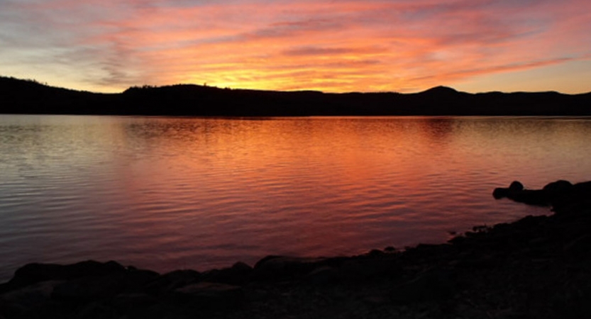 The sky appears in shades of red, orange and purple, and is reflected in the lake below. 